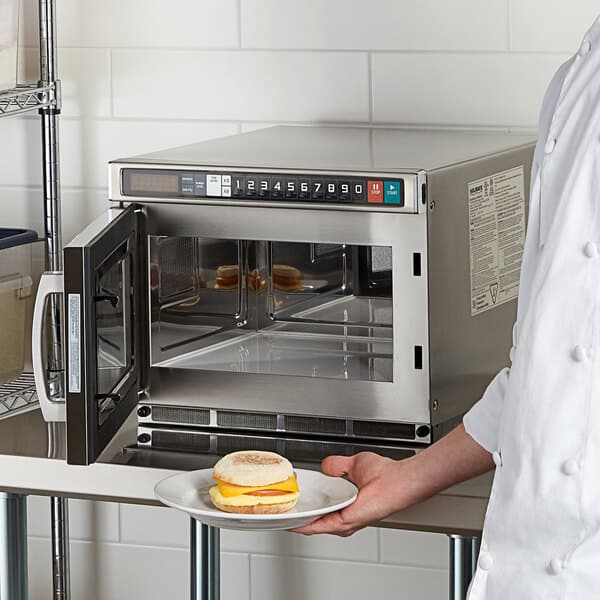 A chef in a white shirt and apron using a Solwave commercial microwave to cook food.