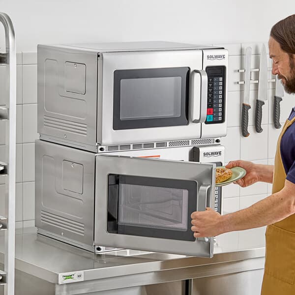 A man in an apron opening a plate of food in a Solwave commercial microwave.